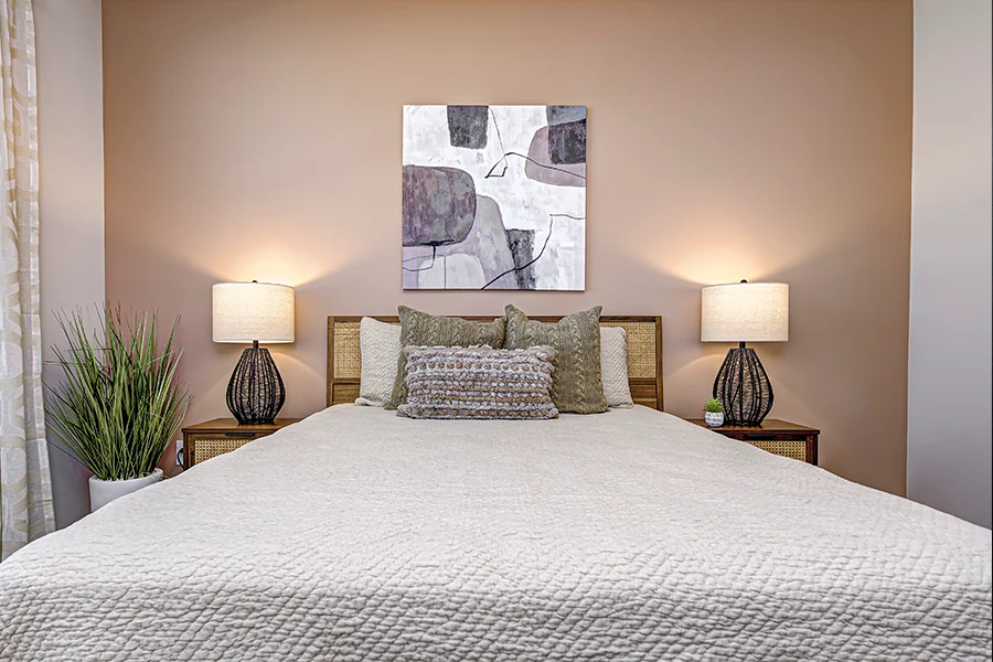 Any apartment space like this bedroom at Wheelhouse Apartments looks better with a little decor. A bed styled with throw pillows, side table lamps, and artwork on the wall